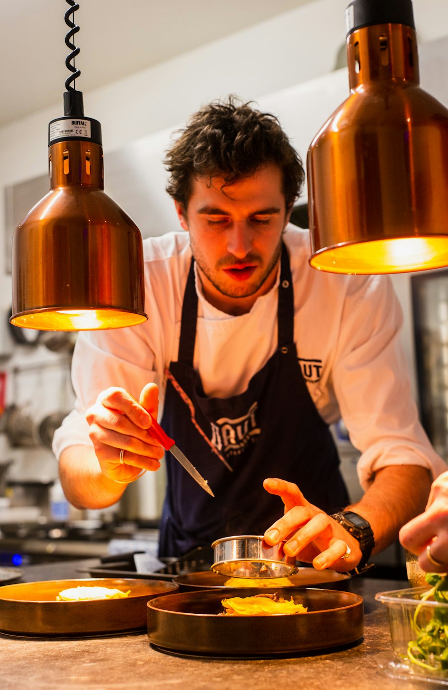 A chef plating food under warm kitchen lights